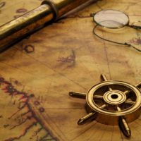 Steering wheel, glasses and spyglass on the old map